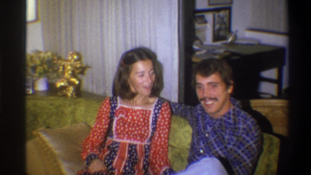 In 1973 Troy, New York home-movie footage, a young couple sit close together on a green couch in a private living room.