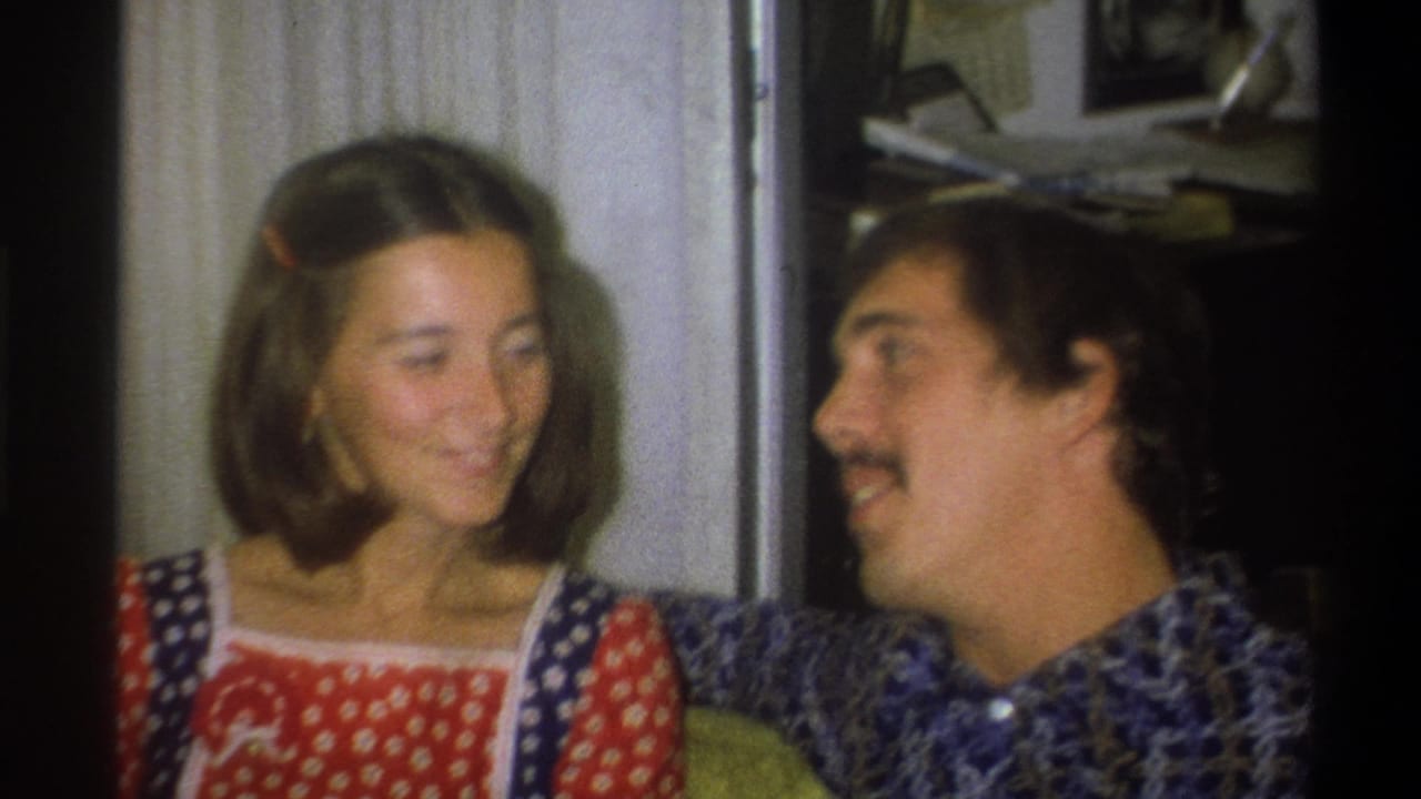 The young woman turns toward the mustached young man during a smiling exchange in the 1973 Troy, New York interior home-movie scene.