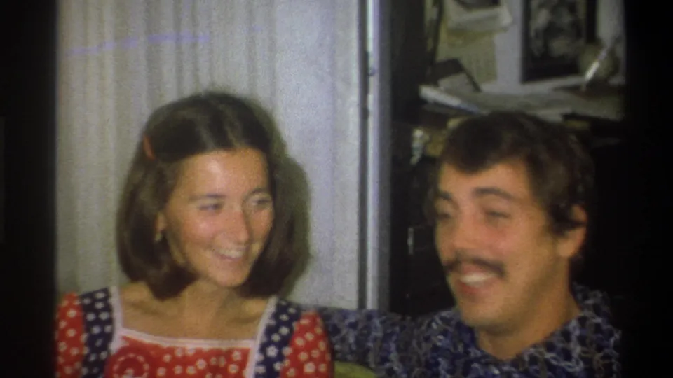 A young woman laughs while seated beside a mustached young man in this 1973 Troy, New York 8mm home-movie frame.