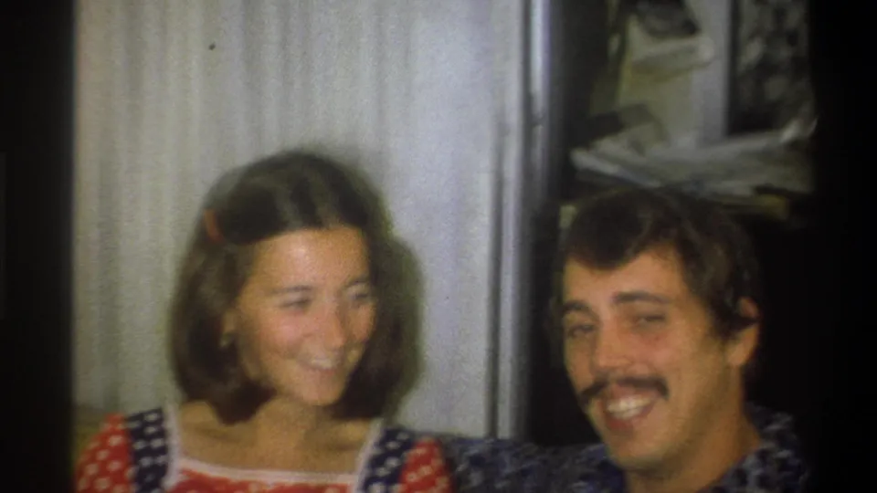 The 1973 Troy, New York home-movie frame shows the young woman and mustached young man smiling together in a private interior.