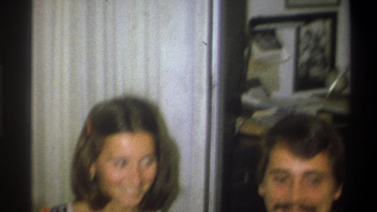 In Troy, New York home-movie footage from 1973, a smiling young woman and man are partly framed in a domestic interior.