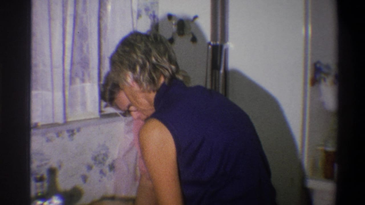 Woman in a dark sleeveless top leans over a kitchen counter near a floral wall pattern.