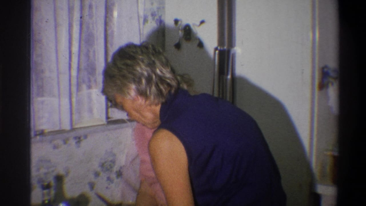 A woman works at the counter in a private 1973 Troy kitchen, with another woman in pink partly visible behind her.
