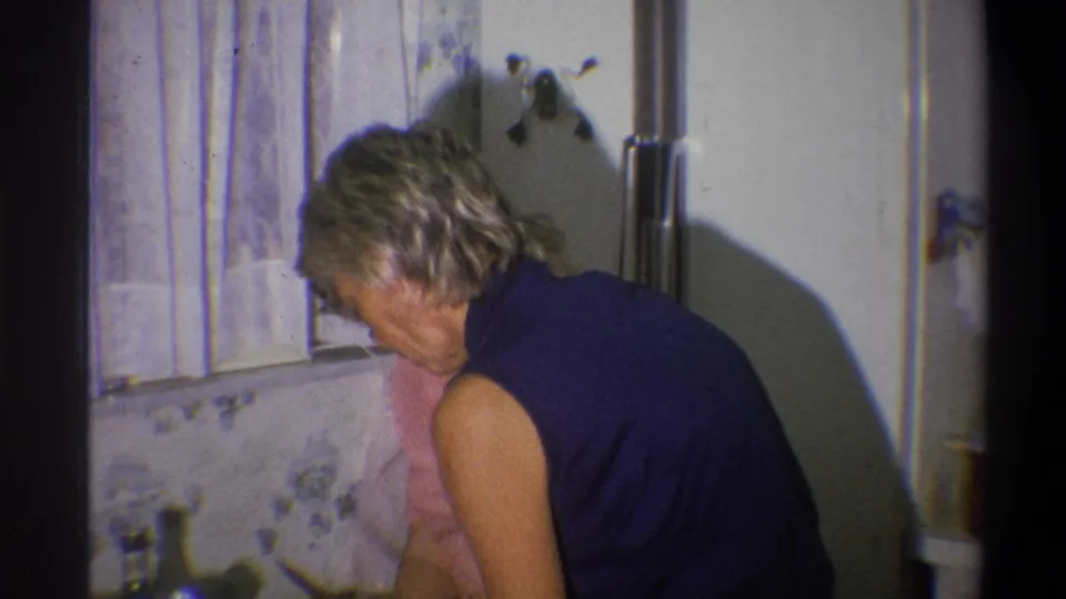 A woman works at the counter in a private 1973 Troy kitchen, with another woman in pink partly visible behind her.
