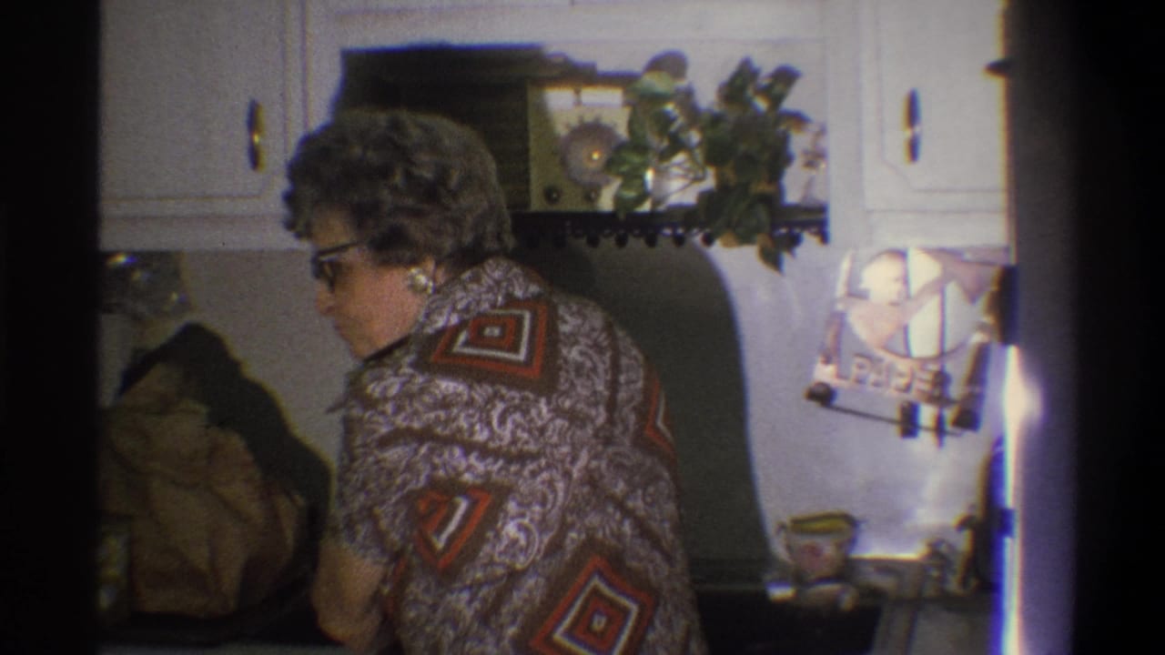 Older woman stands side-on at the kitchen sink, with a wall radio and plant above the counter.