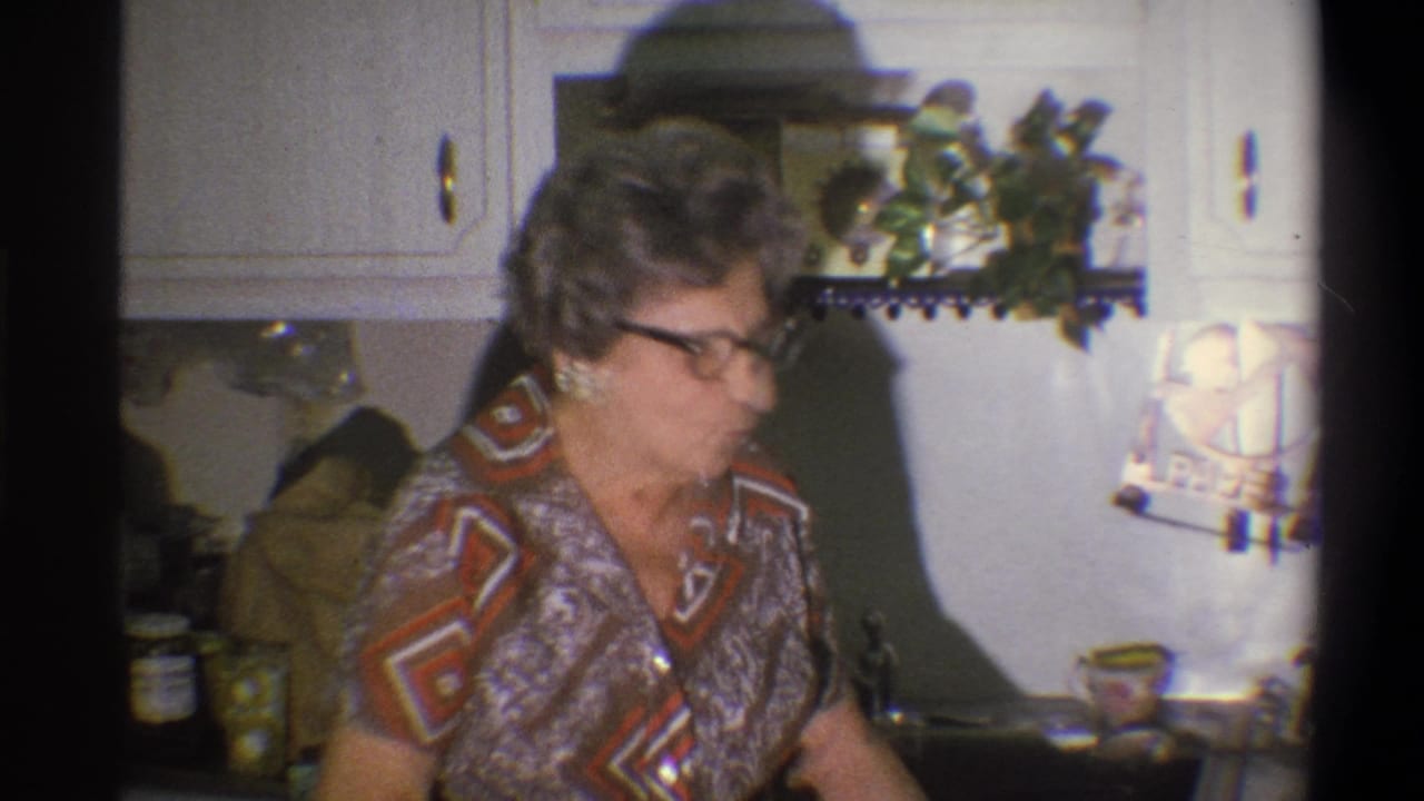 Older woman in glasses standing at a kitchen counter beside white cabinets.