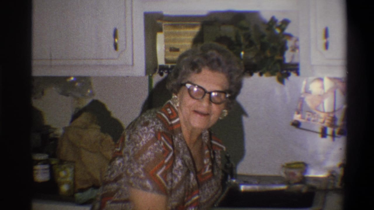 Older woman wearing glasses and earrings looks toward the camera in a 1973 Troy kitchen interior.