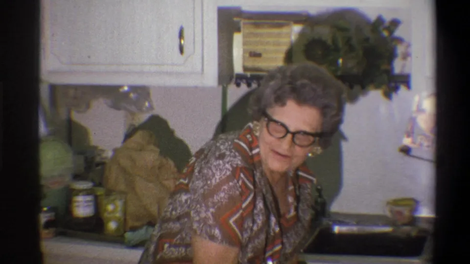 In 1973 home-movie footage from Troy, an older woman leans near the kitchen counter as she appears to speak.