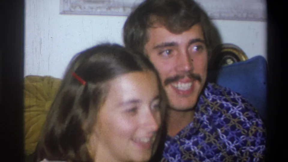 The young couple remains close on the couch as the man glances aside and the woman smiles in the 1973 Troy living-room scene.