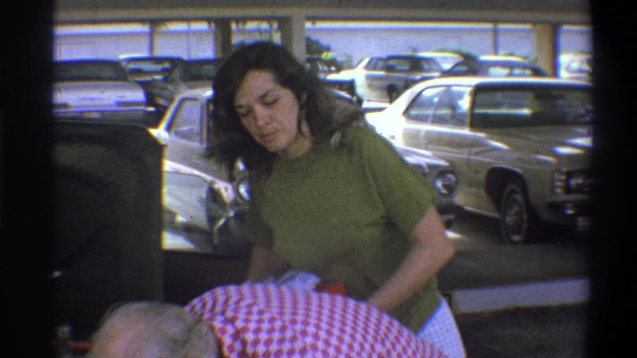 In Troy, New York, 1973 home-movie footage, a woman in a green top stands in a parking garage beside period cars.