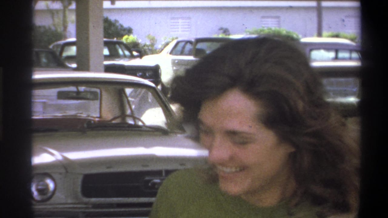 In Troy, New York home-movie footage from 1973, a young woman smiles near parked cars in a public parking area.