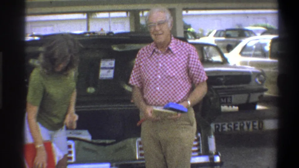In Troy, New York, 1973, two adults appear to load a classic car in a covered parking area before travel.
