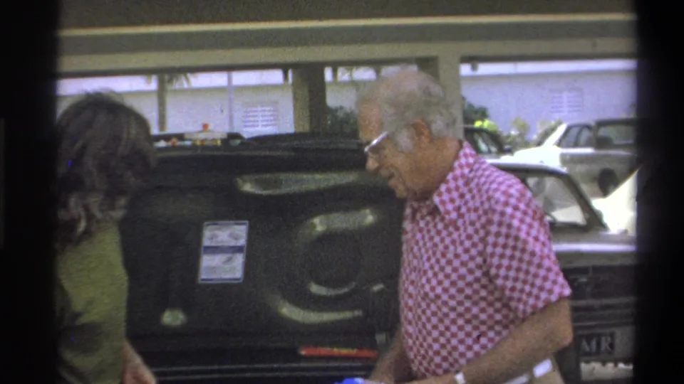 A man and woman work around the open trunk of a classic car in 1973 Troy, New York footage.