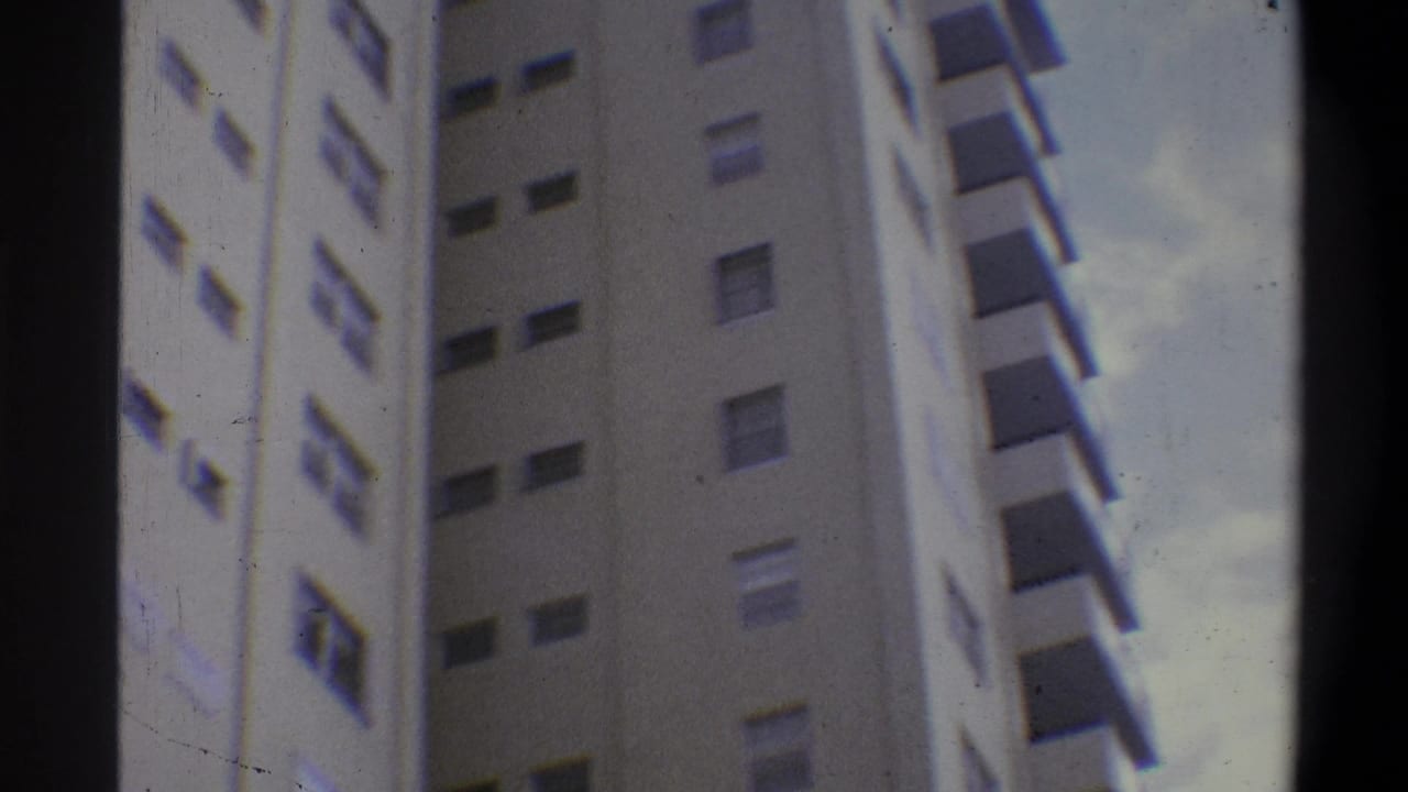 Super 8 low-angle shot of a cream-toned high-rise apartment tower, consistent with early 1970s urban residential architecture in the Troy, New York area.