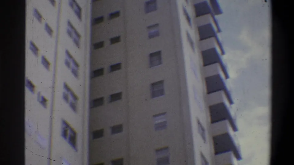 Super 8 low-angle shot of a cream-toned high-rise apartment tower, consistent with early 1970s urban residential architecture in the Troy, New York area.