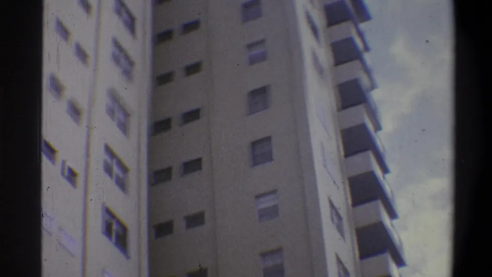 Super 8 low-angle view of residential high-rise with cool color cast and edge color artifact, early 1970s, consistent with Troy, New York area.