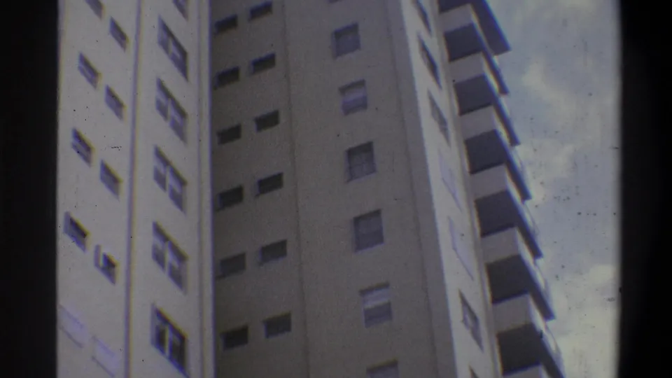 Super 8 low-angle shot of cream-toned residential high-rise with visible film emulsion marks and cool color cast, circa 1973, Troy, New York area.
