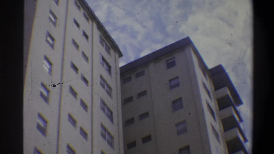 Super 8 low-angle shot showing two cream-colored high-rise apartment towers at a corner junction, early 1970s urban residential setting, Troy, New York area.