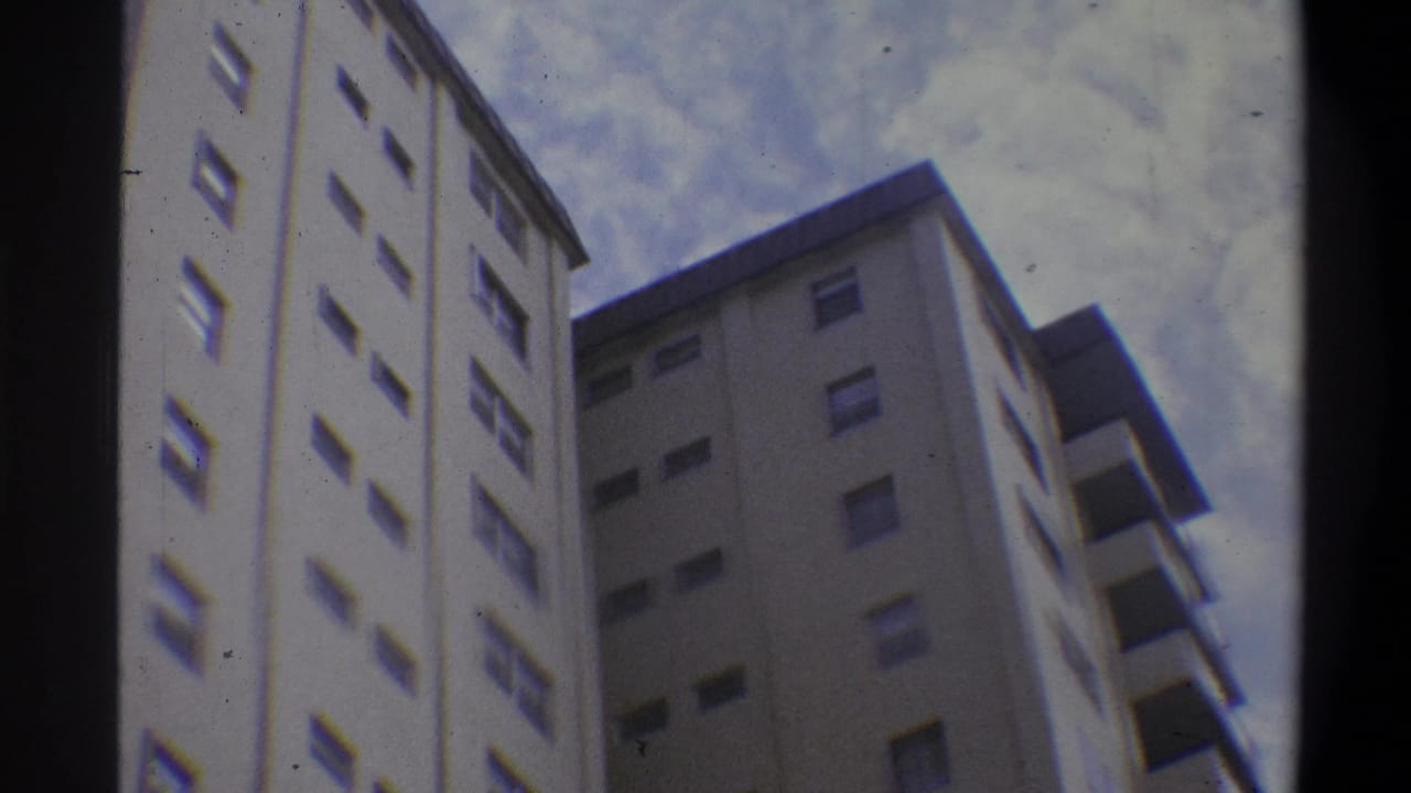 Continued low-angle view of the same off-white apartment towers with repeating windows and balcony overhangs, slightly shifted framing, against a cloudy sky.