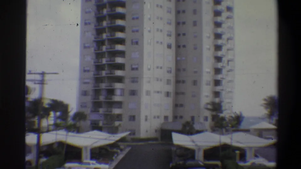 Final 8mm color frame from 1973; the high-rise residential tower occupies the right portion of frame with covered parking canopies and palm trees in the foreground.