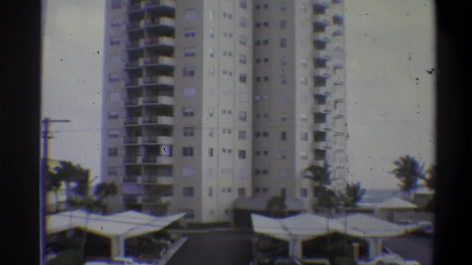 8mm film frame showing the full height of a multi-story residential tower with balcony grid and palm trees; attributed to 1973, location uncertain.