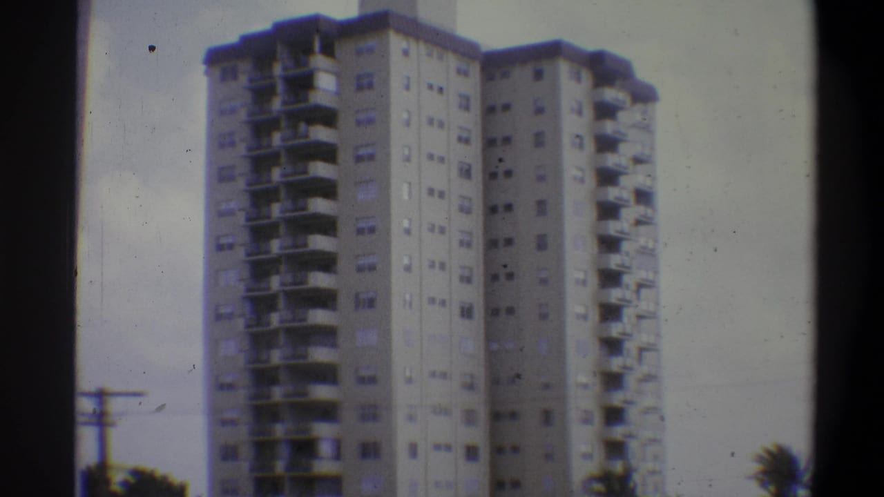 8mm home movie, Troy, New York, 1973 — tall residential tower block against an overcast sky, with a utility pole and tree foliage at the lower left.