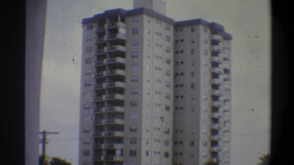 8mm home movie, Troy, New York, 1973 — residential tower seen from a low angle with a utility pole and tree foliage at the base, dense film grain throughout.