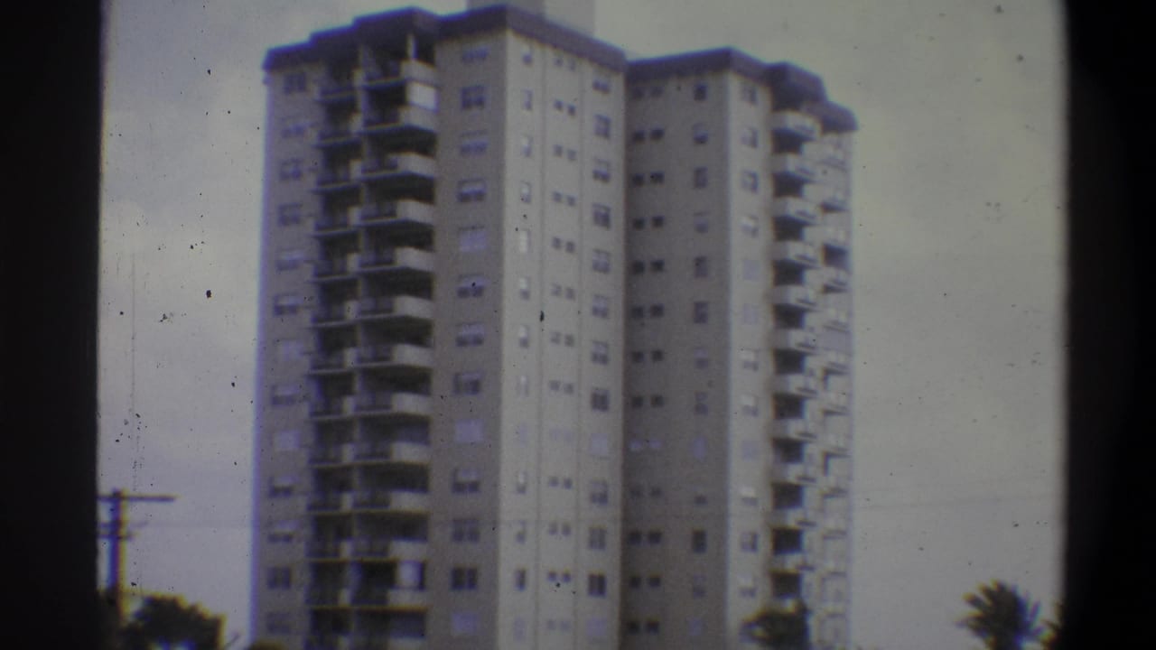 High-rise apartment building, likely Troy New York, 1973 8mm footage; low-angle view shows slab balconies, window grid, utility pole at left, trees at frame edge.