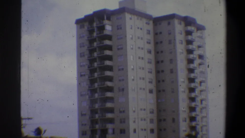1973 8mm shot of high-rise apartment tower, Troy New York area; camera tilt reveals overcast sky above, foliage at lower corners, grain and color shift evident.