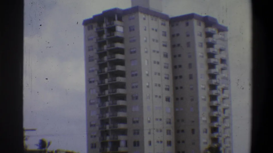 Tall concrete residential tower with horizontal balconies and window grid, Troy, New York area, circa 1973, filmed on 8mm.