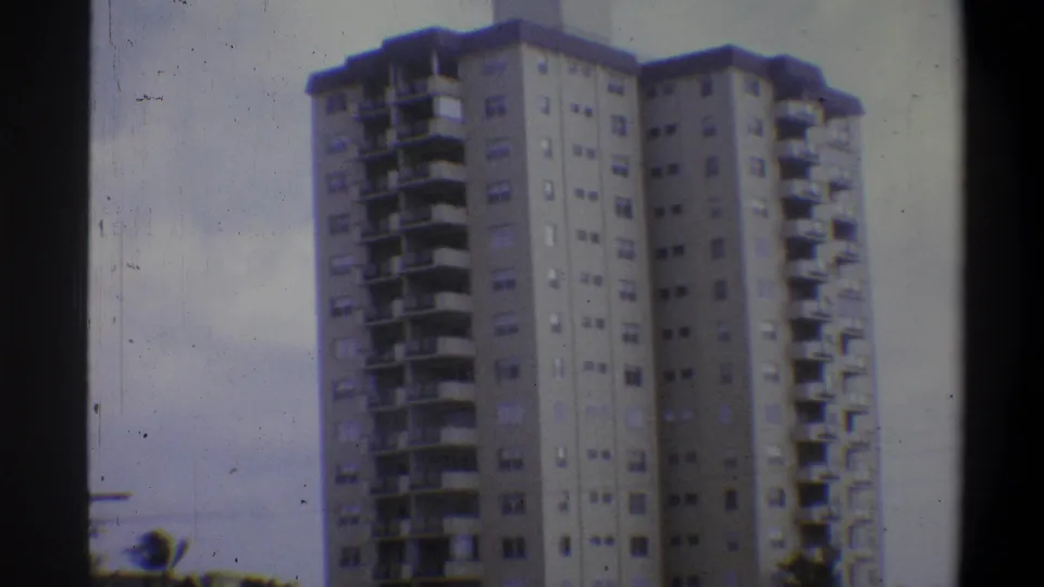 Low-angle view of mid-century concrete apartment tower with foliage in foreground, circa 1973 Troy, New York area, 8mm.