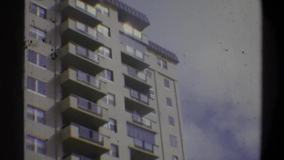 Close upward view of the top floors and rooftop penthouse of a modernist concrete apartment building on 8mm film, Troy, New York, c. 1973.