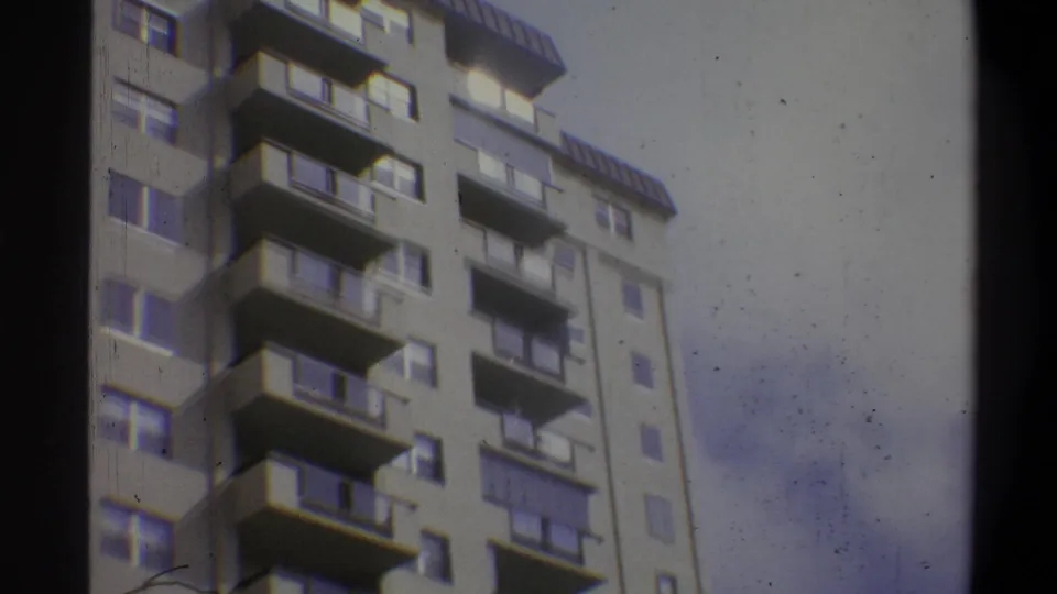 Final frame of 8mm upward pan showing a concrete apartment tower with cantilevered balconies and rooftop structure, overcast sky at right, Troy, New York, c. 1973.
