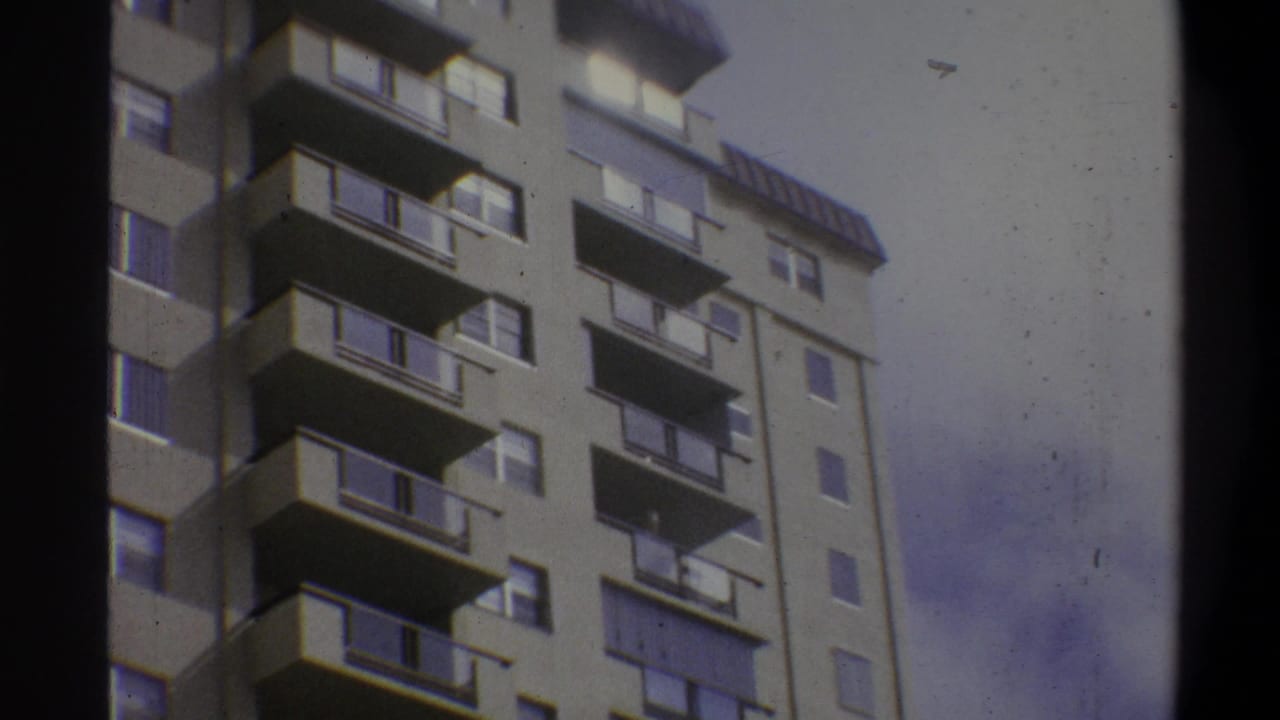 Low-angle 8mm home-movie shot of a concrete high-rise apartment building in Troy, New York, circa 1973, showing repeating balconies and large windows.