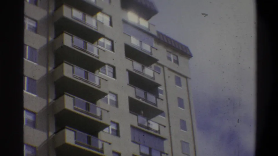 Low-angle 8mm home-movie shot of a concrete high-rise apartment building in Troy, New York, circa 1973, showing repeating balconies and large windows.