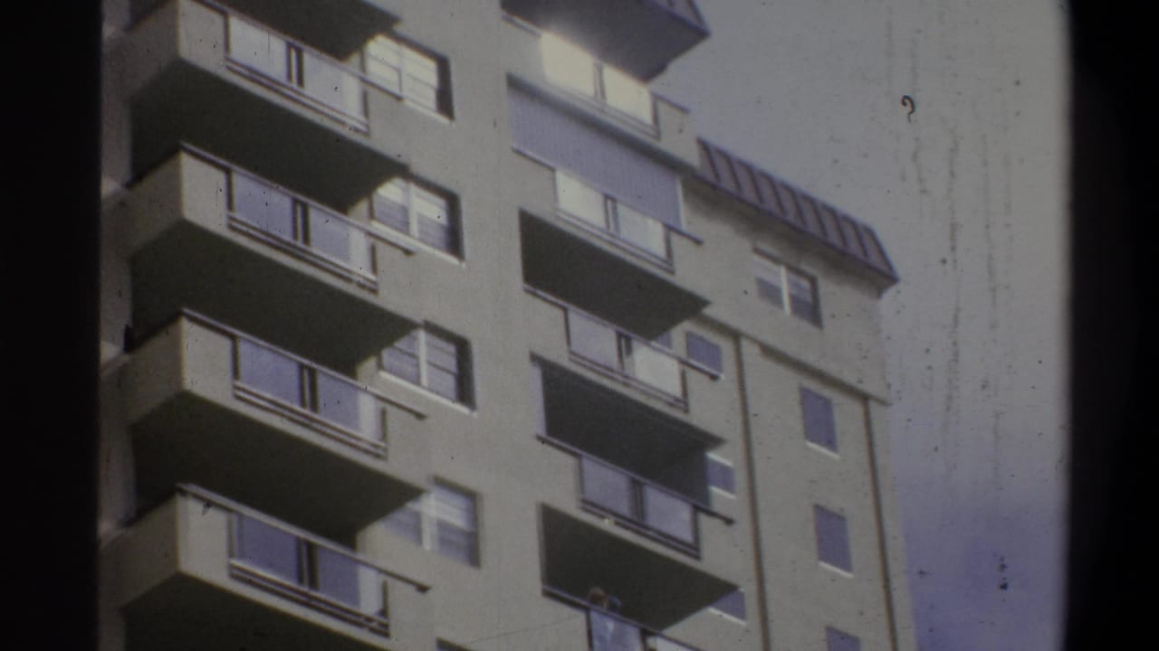 8mm home-movie upward view of a concrete apartment high-rise, likely Troy, New York, circa 1973, with cantilevered balconies and a rooftop horizontal louver structure.