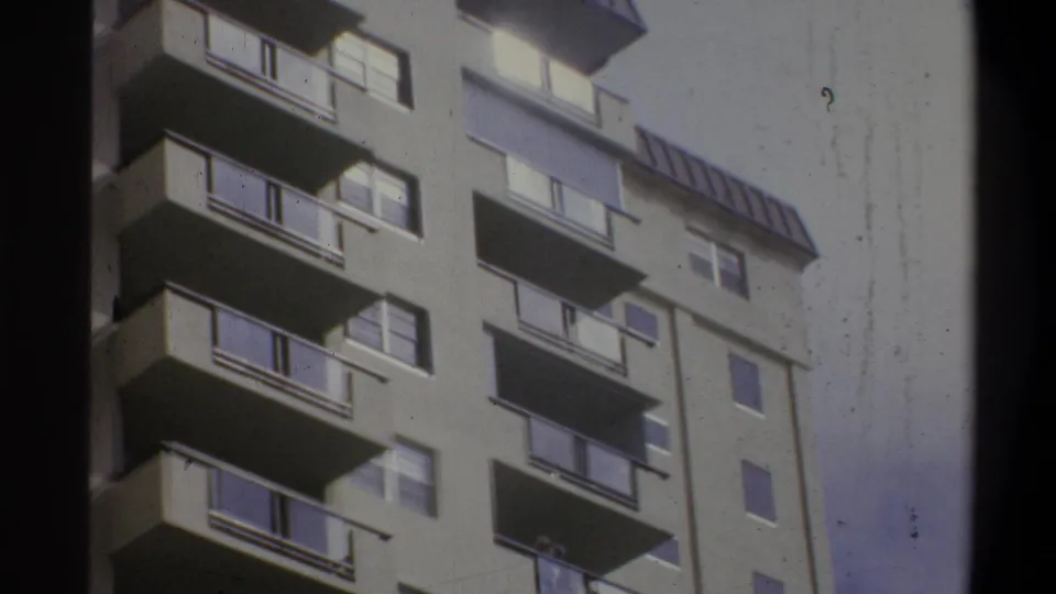 8mm home-movie upward view of a concrete apartment high-rise, likely Troy, New York, circa 1973, with cantilevered balconies and a rooftop horizontal louver structure.