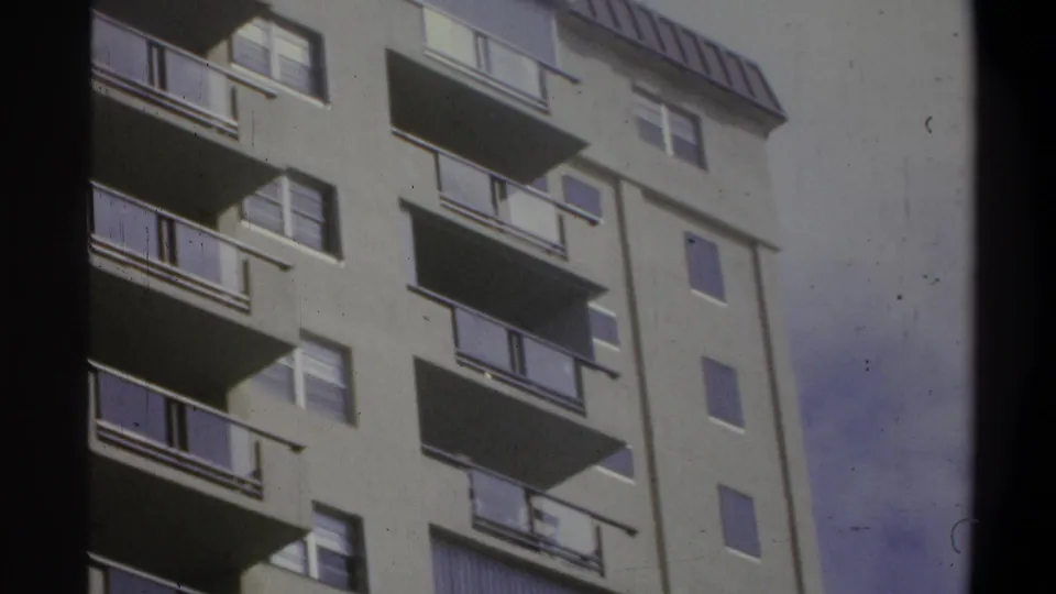 8mm home-movie low-angle view of a concrete residential high-rise, Troy, New York, circa 1973, with a uniform balcony and window grid against a pale sky.