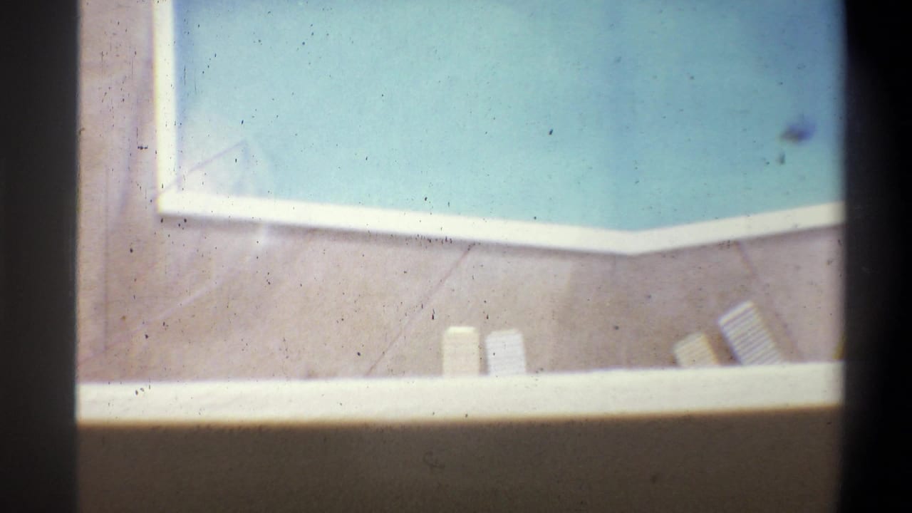 Overhead 8mm shot of a hotel swimming pool with white-tiled coping and poolside lounge chairs, shot from an upper floor, circa 1973.