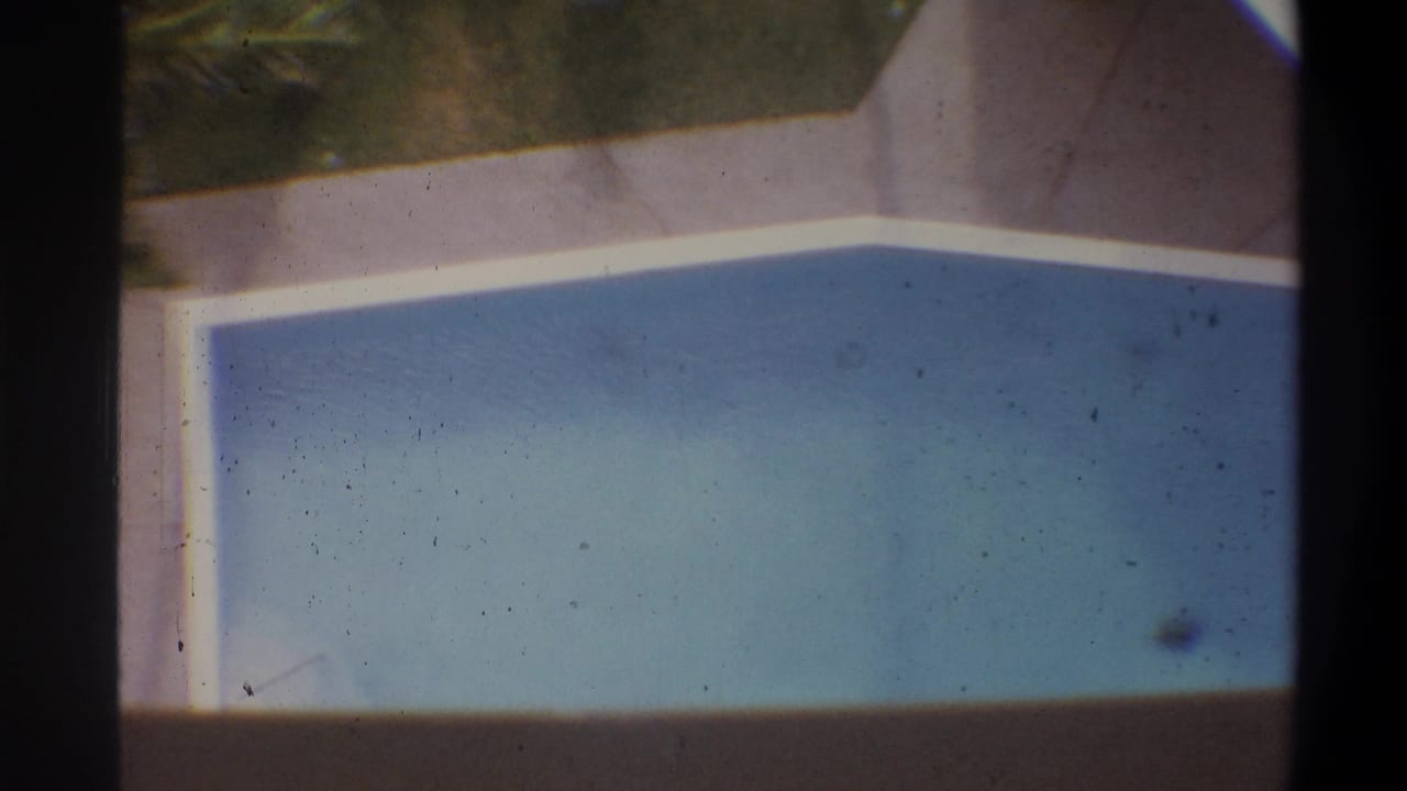 Overhead 8mm home-movie shot of a rectangular blue swimming pool with white-coped edges at what appears to be a tropical vacation property, circa 1973.