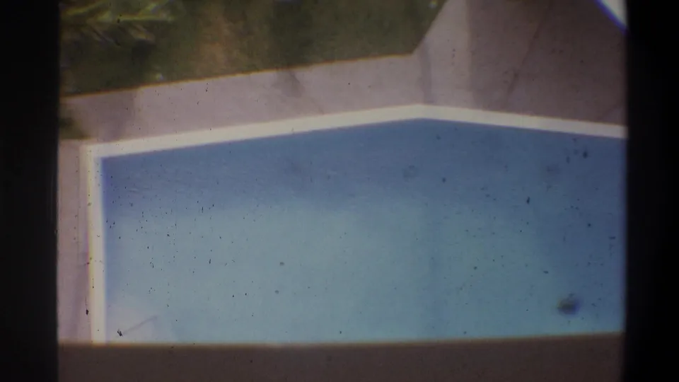 Overhead 8mm home-movie shot of a rectangular blue swimming pool with white-coped edges at what appears to be a tropical vacation property, circa 1973.