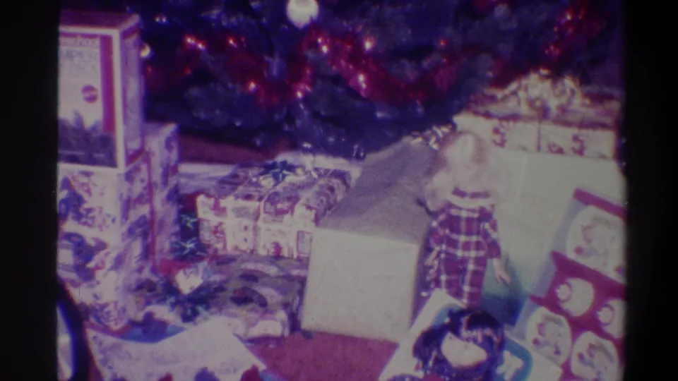 8mm home movie, 1973, Troy NY: mid-pan frame showing Christmas gifts beneath tree, branded toy box at top centre, flat wrapped package at right.