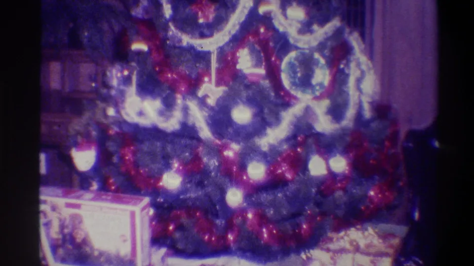 Christmas tree mid-to-lower section in a 1973 Troy NY living room — red tinsel, silver garland swags, round ornaments, and wrapped presents on the floor beneath.