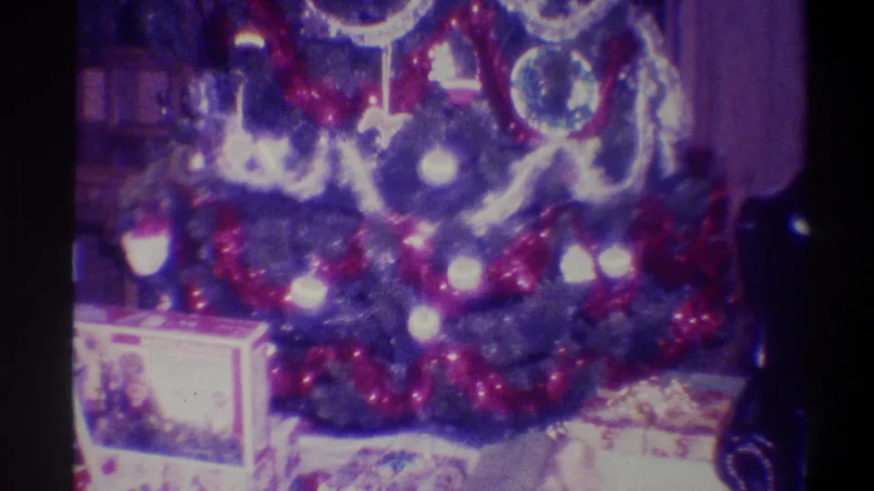 Christmas tree base and gifts in a 1973 Troy NY living room — red tinsel, silver garland, large glass-ball ornaments, and gift boxes on the floor; 8mm purple dye-fade.