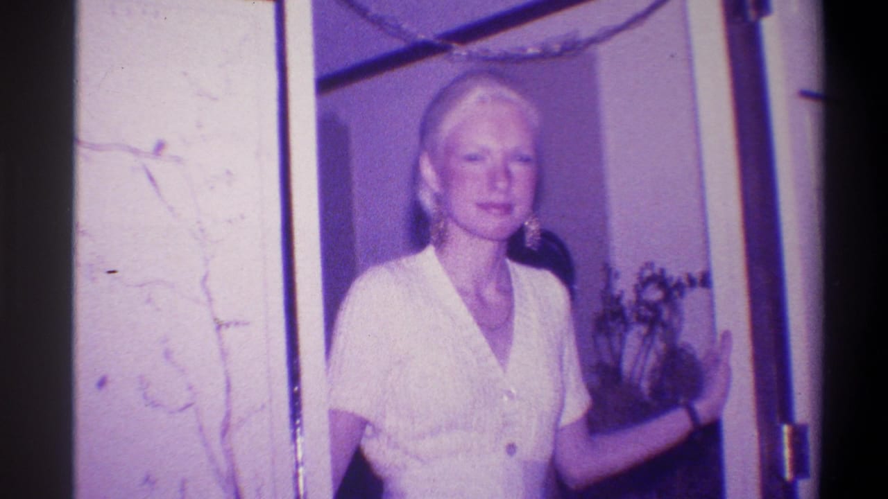 Blonde woman in white short-sleeve top stands in a doorway, posing for a photograph