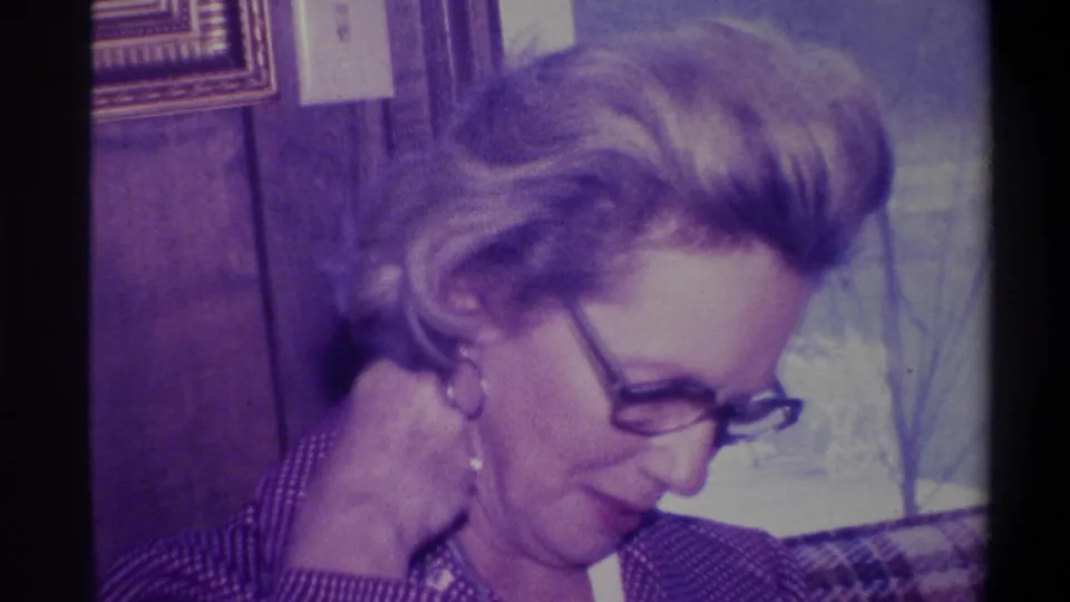 Woman with styled bouffant hair looking down, dark-rimmed glasses and earring visible, wood-paneled domestic interior, Troy, New York, circa 1973