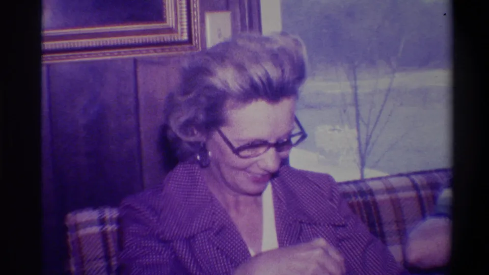 Close-up of woman in 1970s-style dark-framed glasses and purple jacket looking down at gift contents with a pleased expression, Troy, New York, circa 1973.