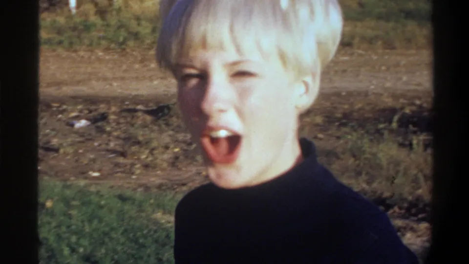 Young woman with short blonde hair turning to face camera, mouth open mid-expression, dark turtleneck — candid 8mm moment, circa 1974, Gainesville, Florida.