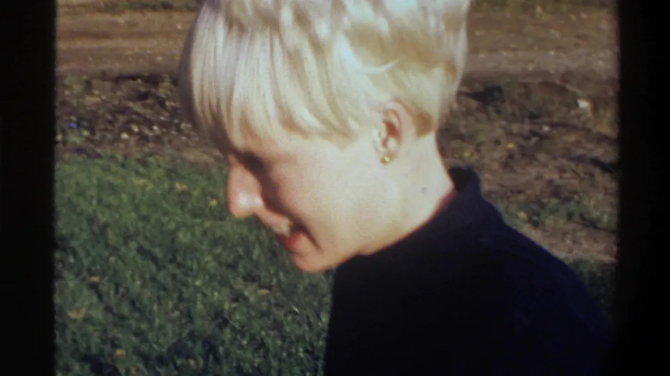 Young woman in right-side profile, small stud earring clearly visible, short blonde hair, dark turtleneck — 8mm home movie, circa 1974, Gainesville, Florida.