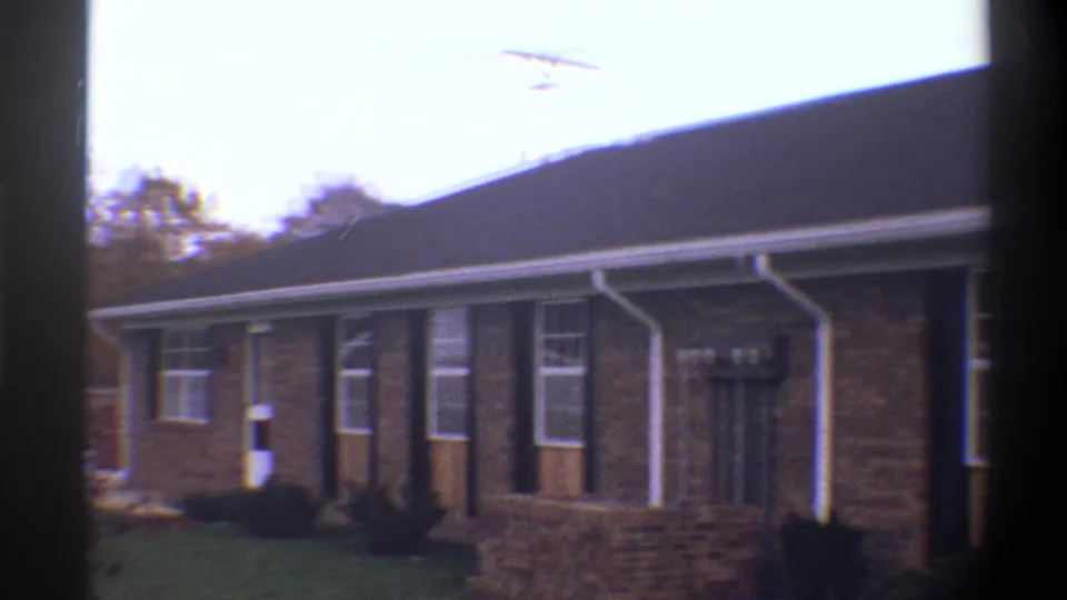 Wider 8mm shot of a 1974 Gainesville, Florida brick ranch house; roof-mounted TV antenna and background trees visible.